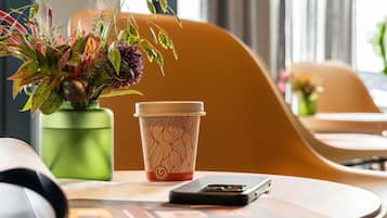 A workspace with a green plant, a patterned cup, and a smartphone on a table.