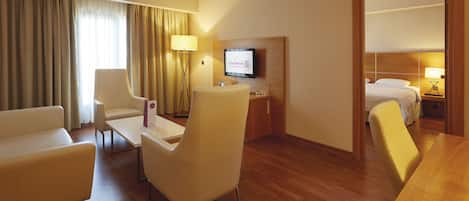 Habitación de hotel con suelo de madera, cama, escritorio con televisor, silla y sofá.
