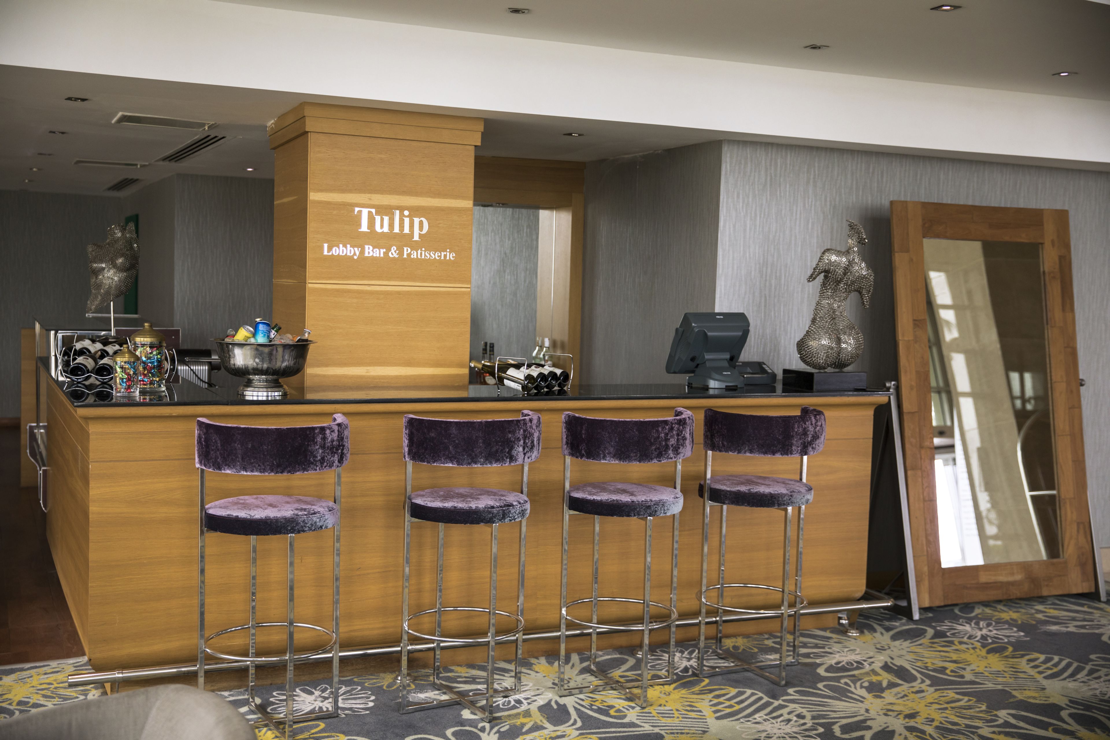 A bar area with a wooden counter, four purple bar stools, and a mirror.