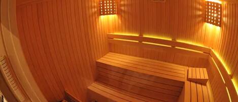 Un sauna avec des bancs et des murs en bois, équipé de radiateurs fixés au mur et d’un radiateur intégré à un banc.