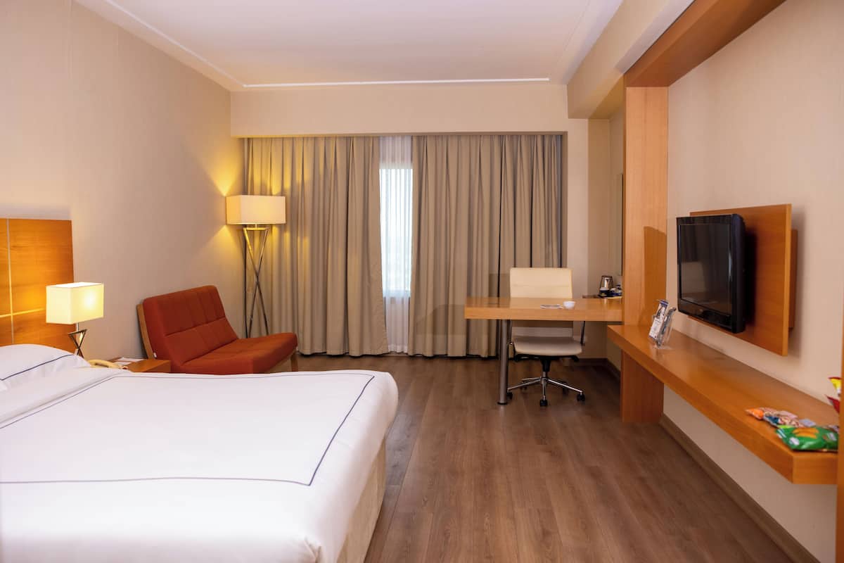 Una habitación de hotel con una cama, un escritorio, una silla, un televisor y una lámpara.