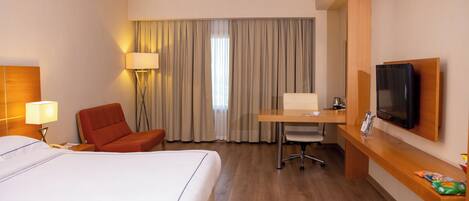 A hotel room with a bed, a desk, a chair, a TV, and a lamp.