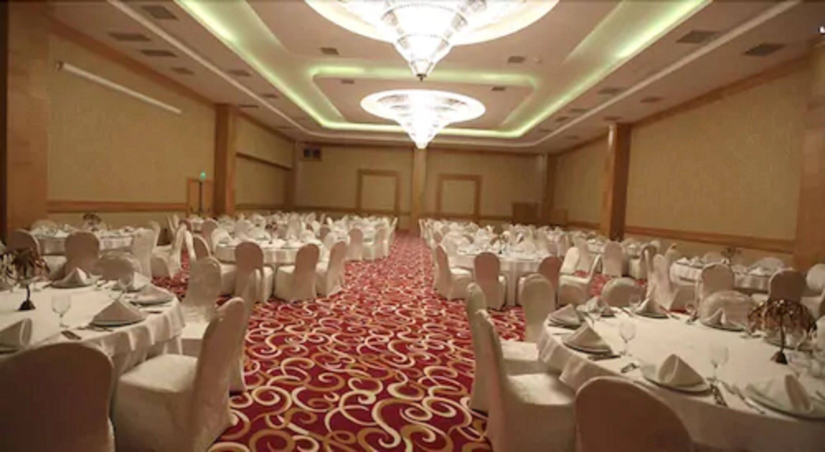 A banquet hall with round tables, white chairs, and a red carpet.