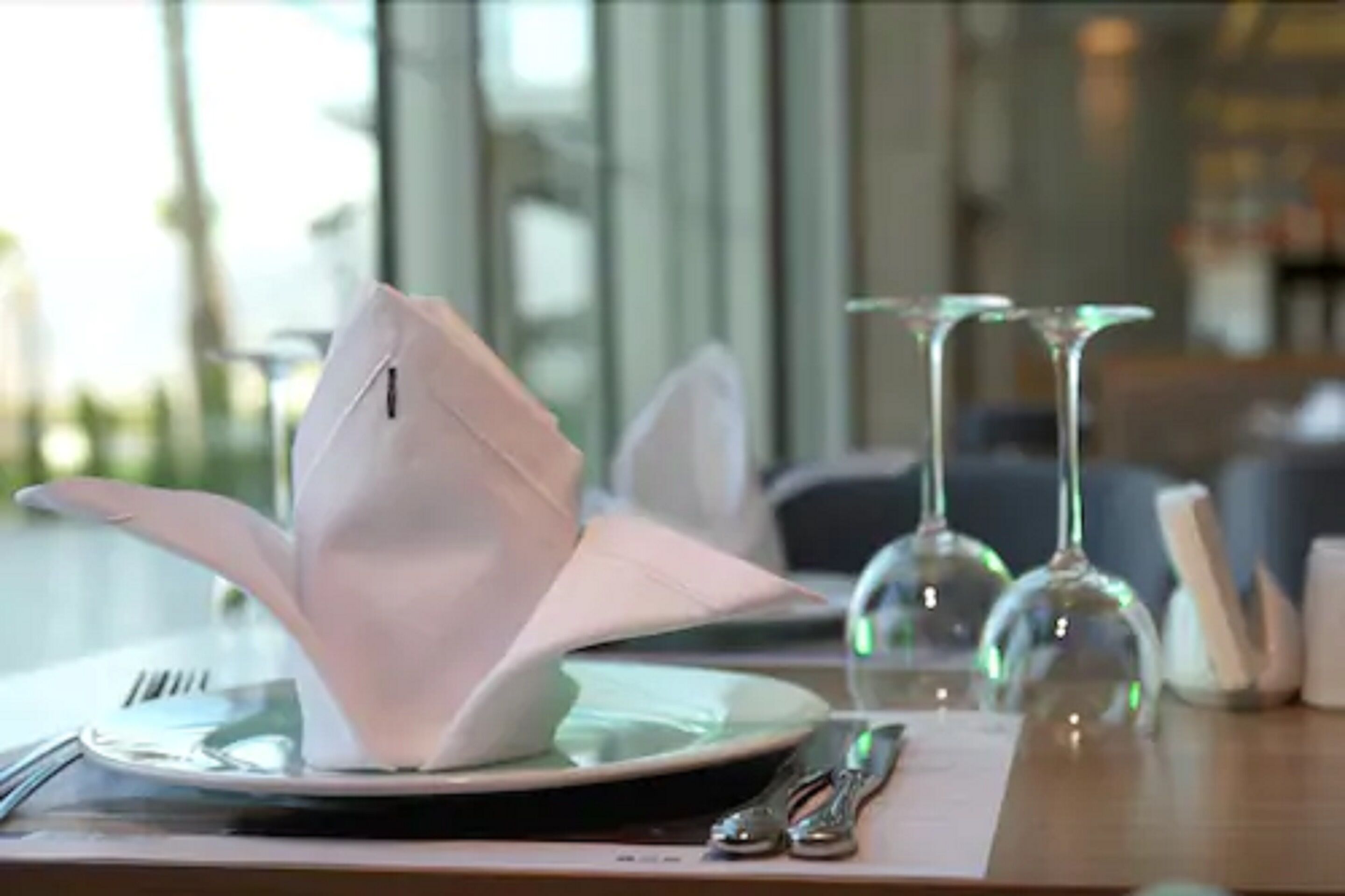 A dining table set with a white napkin, a plate, a fork, a knife, and two wine glasses.