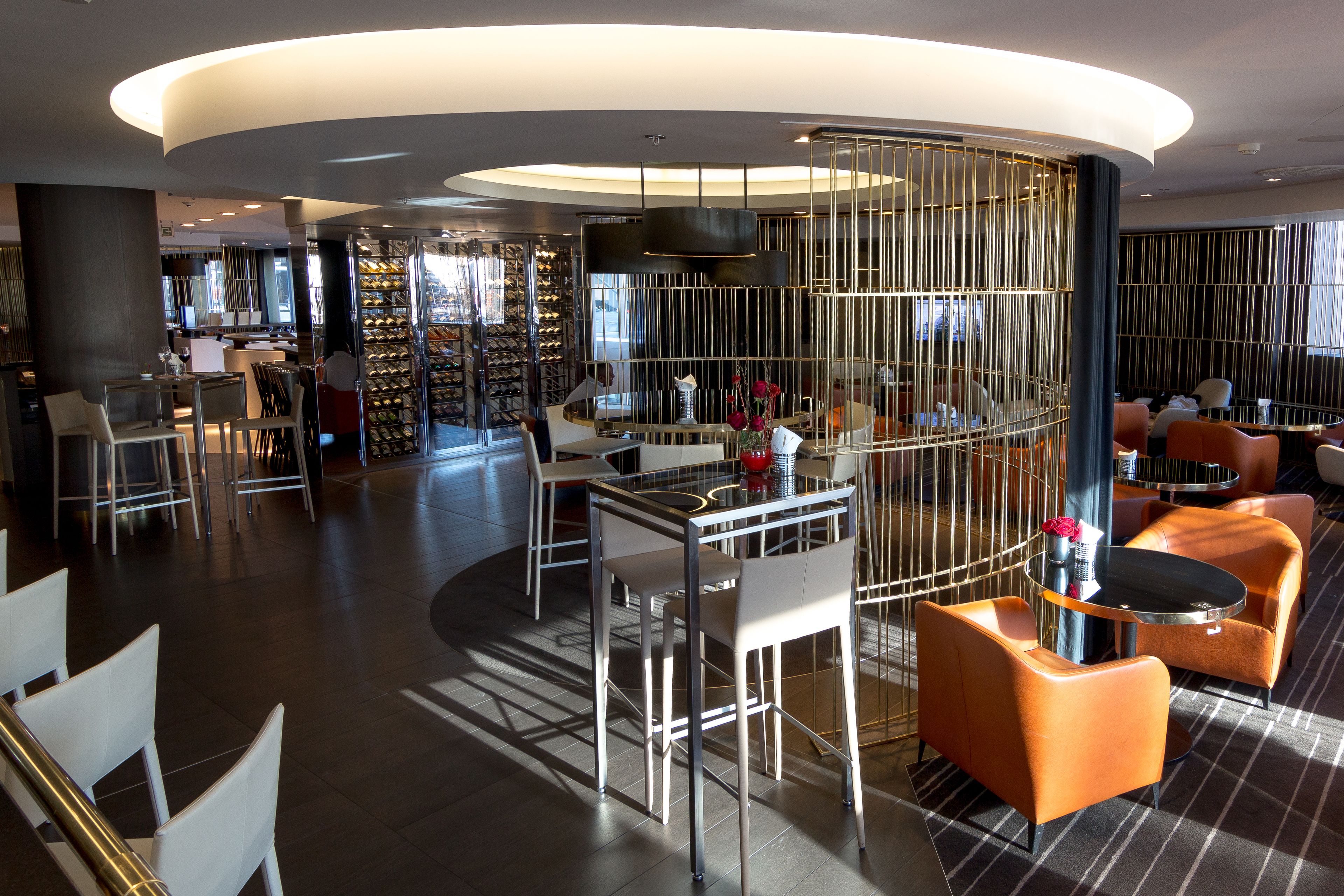 A modern hotel lobby with a central bar area, seating arrangements, and a wine display.