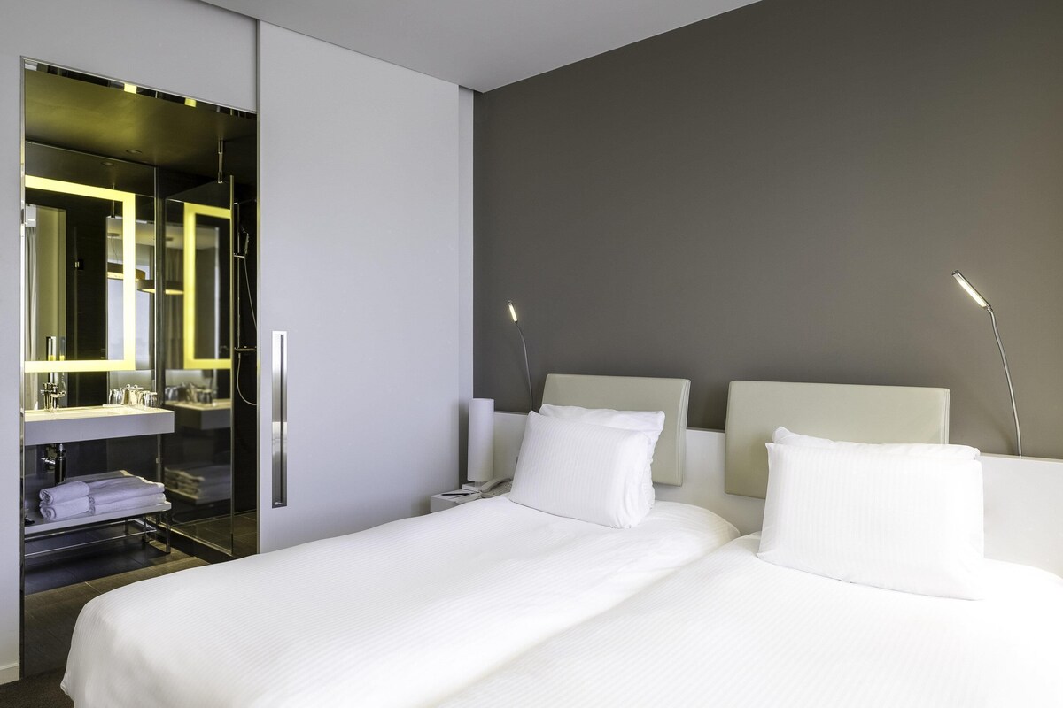 Habitación de hotel con cama, mesita de noche, lámpara, espejo y armario.