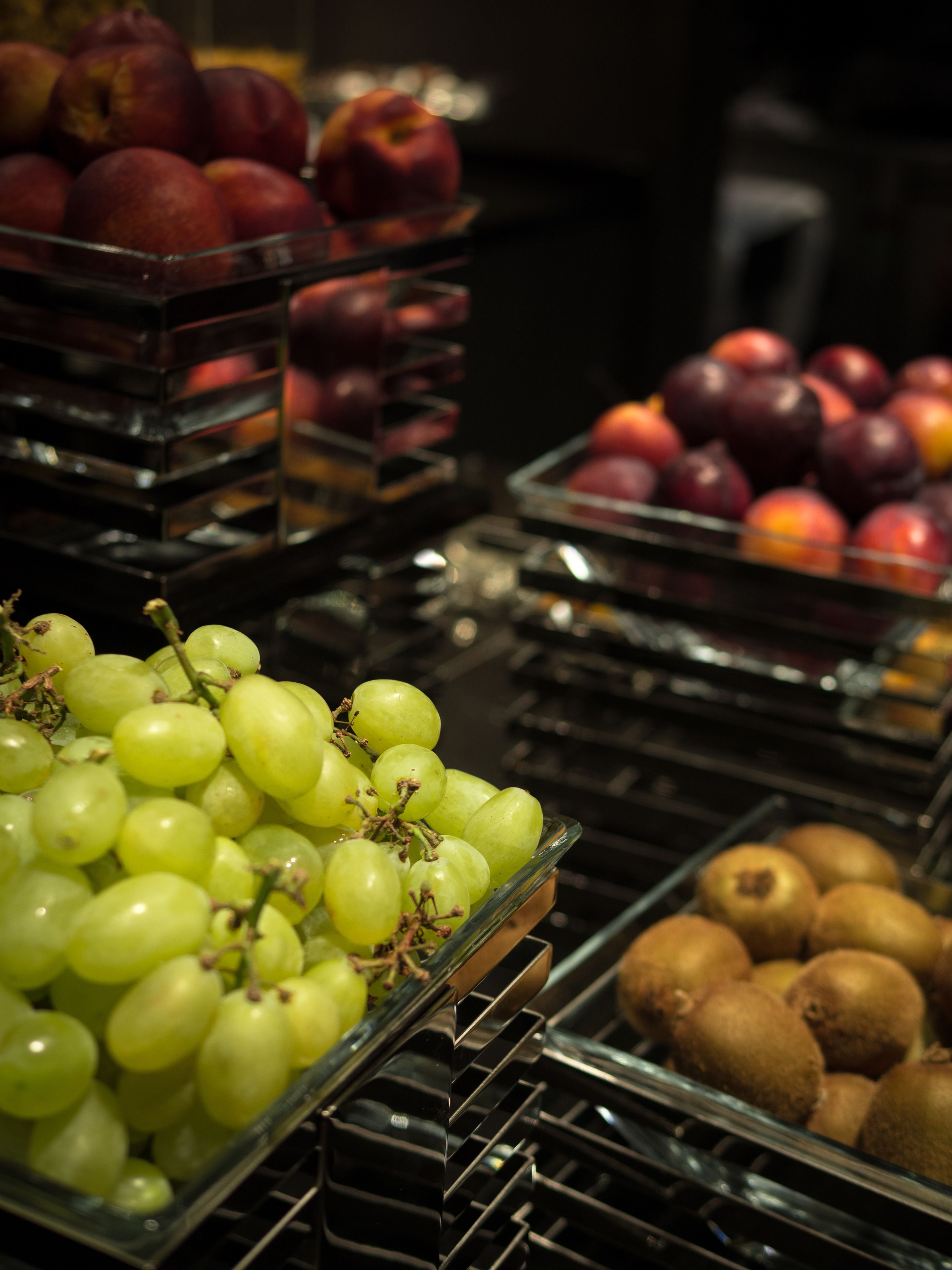 Exposição de diversas frutas, incluindo maçãs, uvas e kiwis em uma loja.
