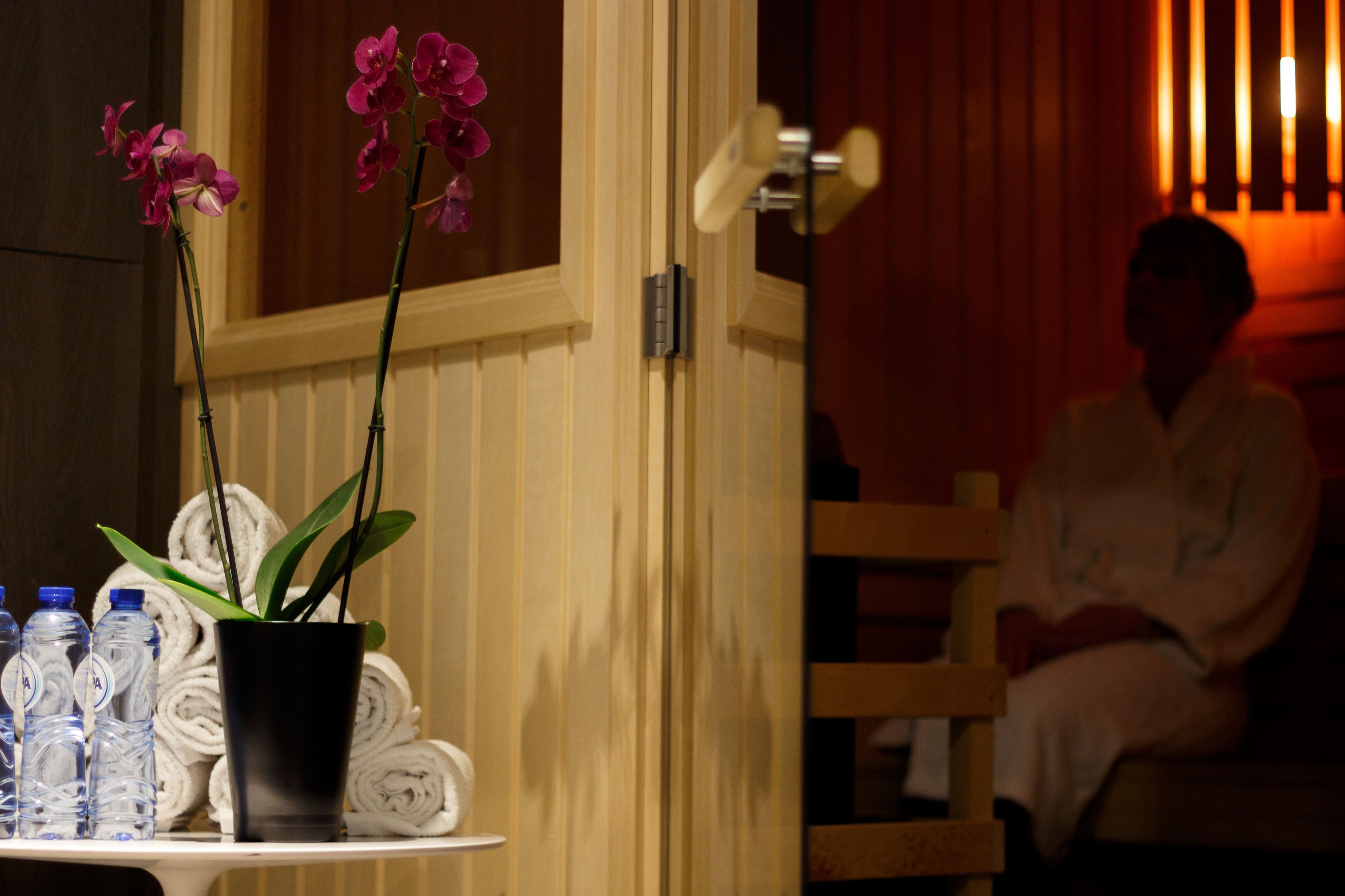 Un cuarto de spa con una puerta de madera, una orquídea en maceta, toallas enrolladas y agua embotellada sobre una mesa.