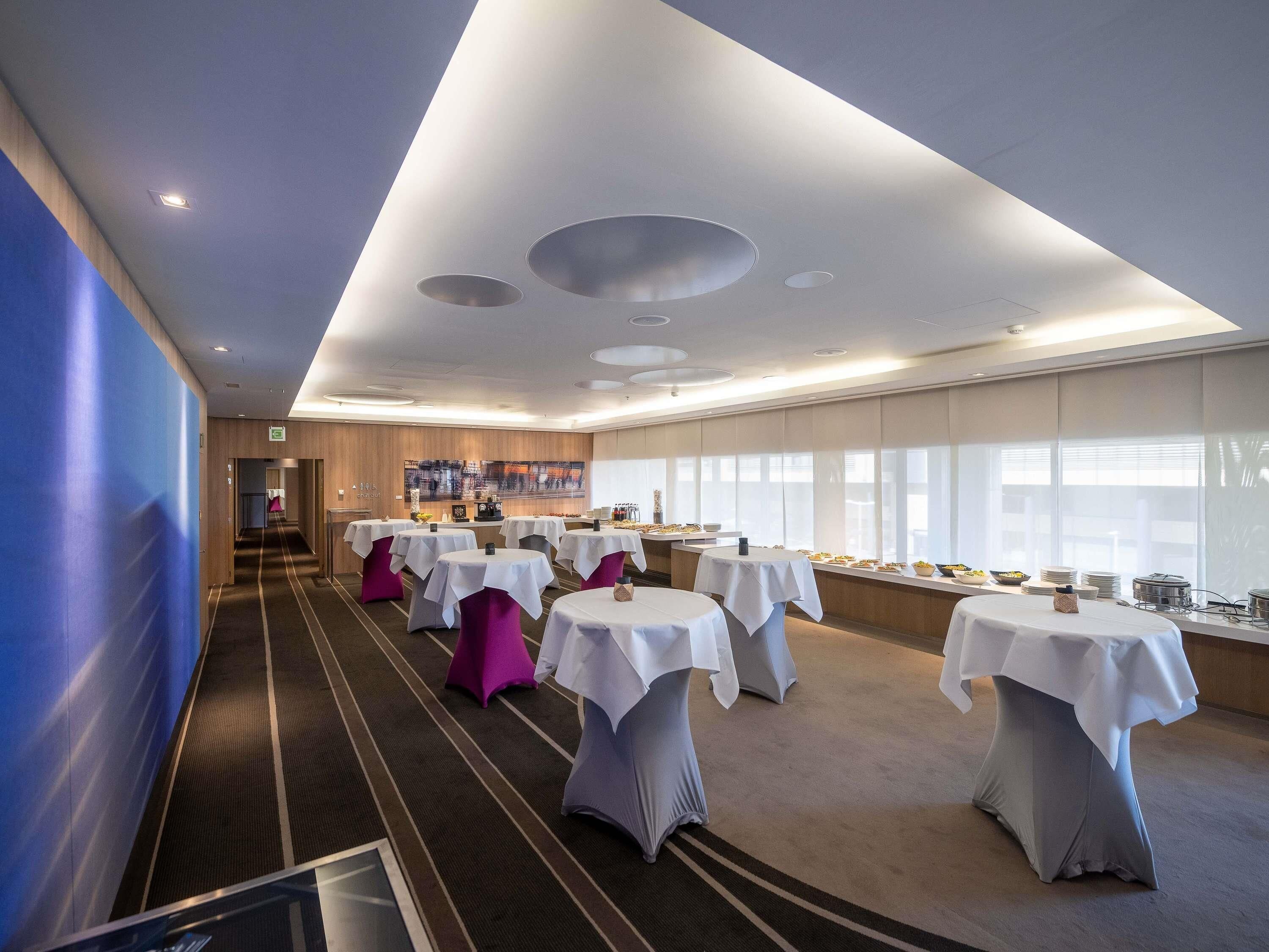 A hotel conference room with multiple tables, a long corridor, and a large window.