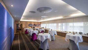 A hotel conference room with multiple tables, a long corridor, and a large window.