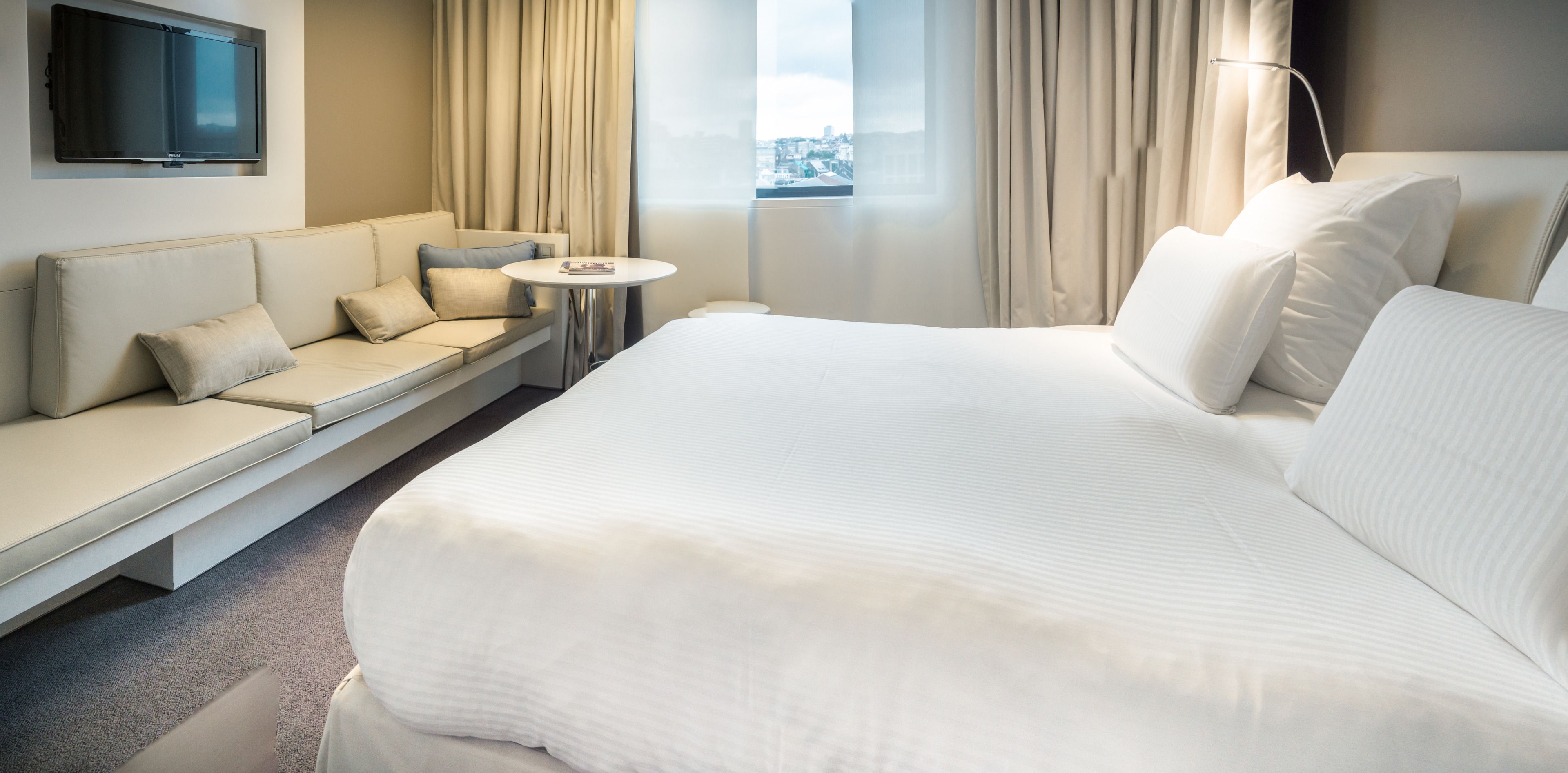 Une chambre d’hôtel avec un grand lit, un canapé, une petite table et un téléviseur fixé au mur.