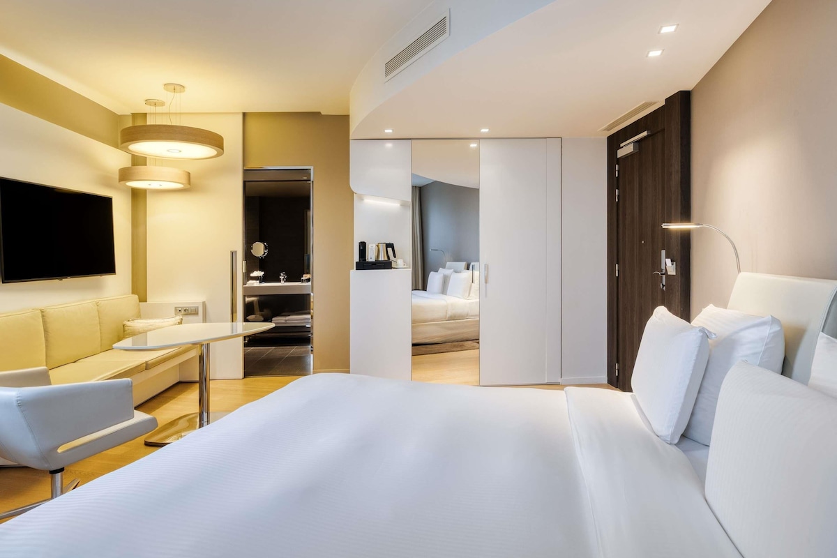 Una habitación de hotel moderna con una cama grande, un escritorio, una silla, un televisor y un armario.