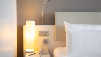 Een net opgemaakt bed met witte lakens, een bedlamp, een telefoon en een lichtschakelaar aan de muur.