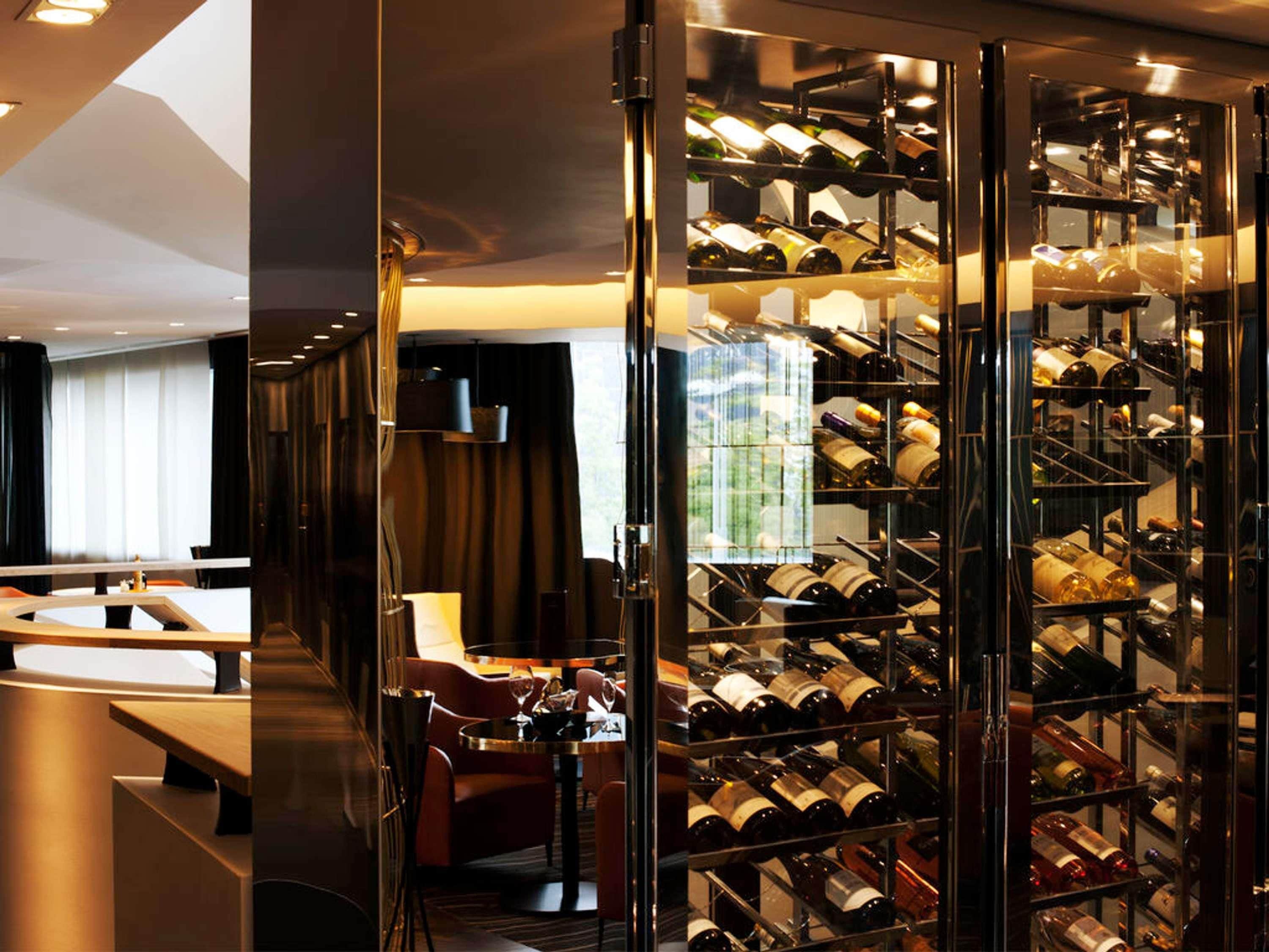 A hotel room with a wine cellar, a dining area, and a view of the cityscape.