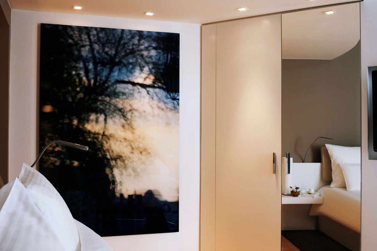 Una habitación de hotel moderna con un cuadro abstracto grande, una cama, una mesita de noche y un armario.