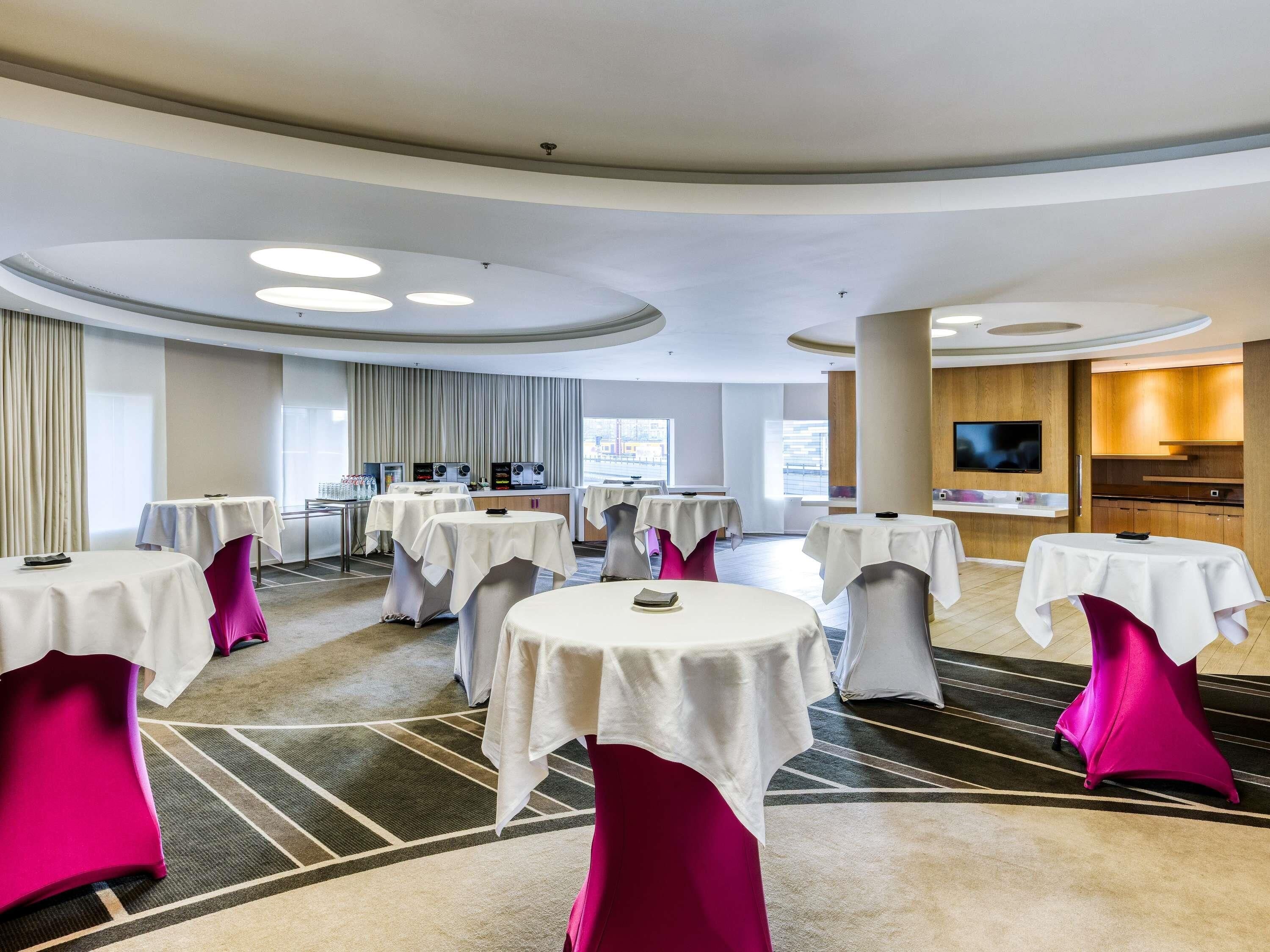 A conference room with multiple tables, a kitchen area, and a television.