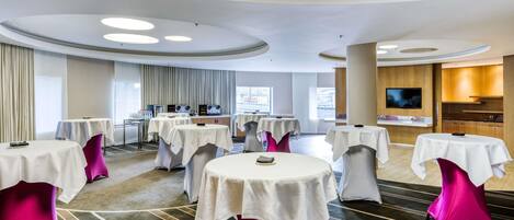 A conference room with multiple tables, a kitchen area, and a television.