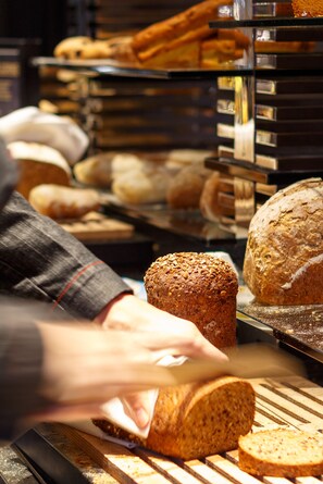 Una vetrina di panetteria con diversi tipi di pane e una persona che affetta una pagnotta.
