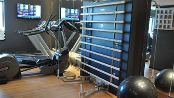 Een fitnessruimte met trainingsapparatuur, waaronder loopbanden en een wandrek.