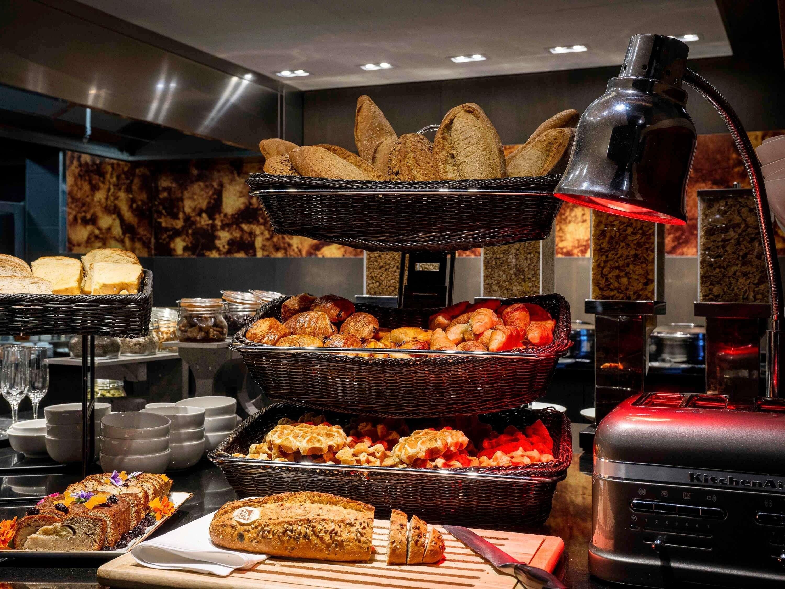 A buffet with various breads and pastries, a cutting board with a knife, and a kitchen appliance in the background.