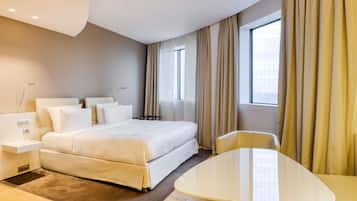 Ein modernes Hotelzimmer mit einem Bett, Nachttischen, einem Schreibtisch und einem Fenster mit Vorhängen.