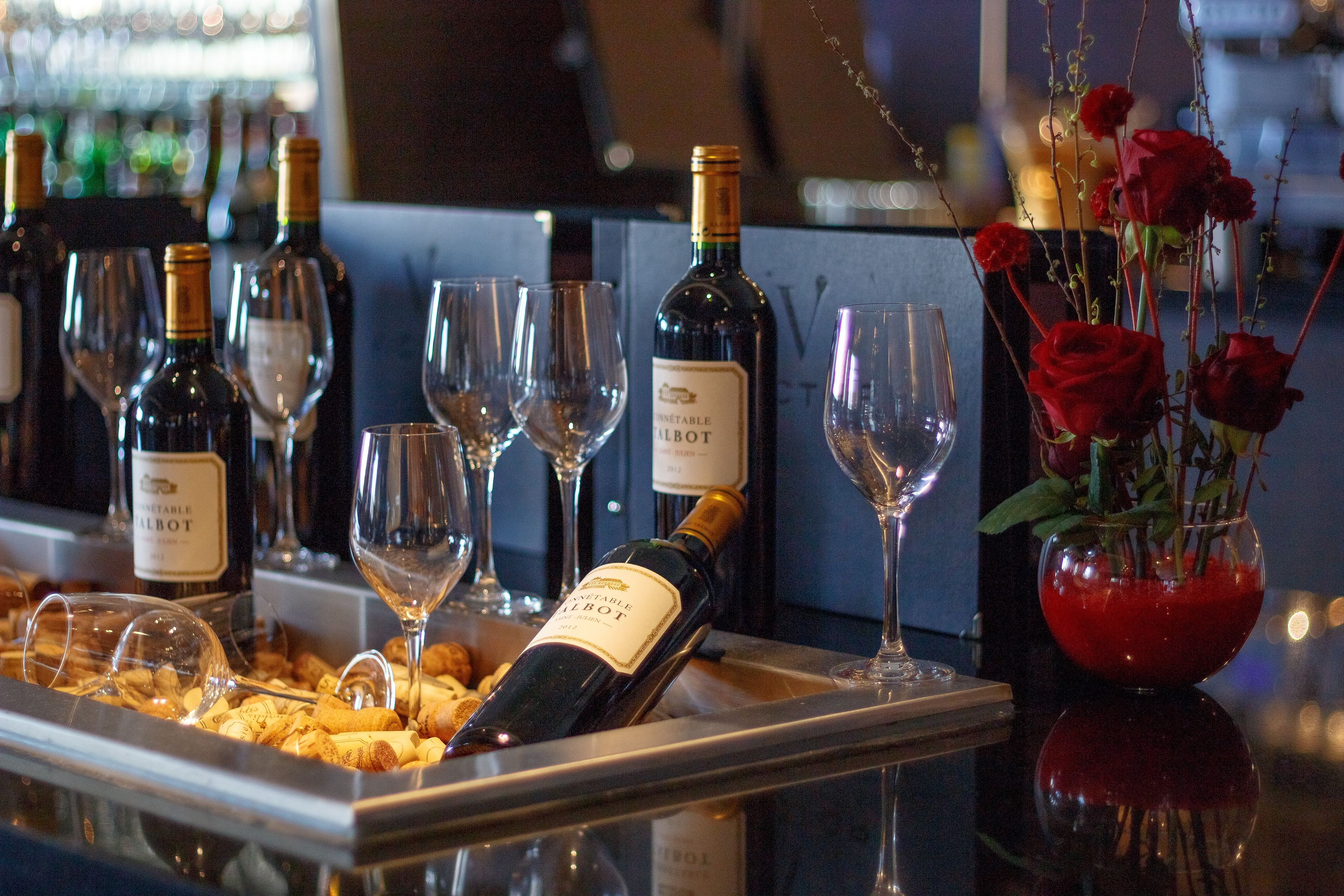 Une présentation de vins avec des bouteilles et des verres, un vase rempli de roses rouges et une bouteille de vin « Pinot Noir ».