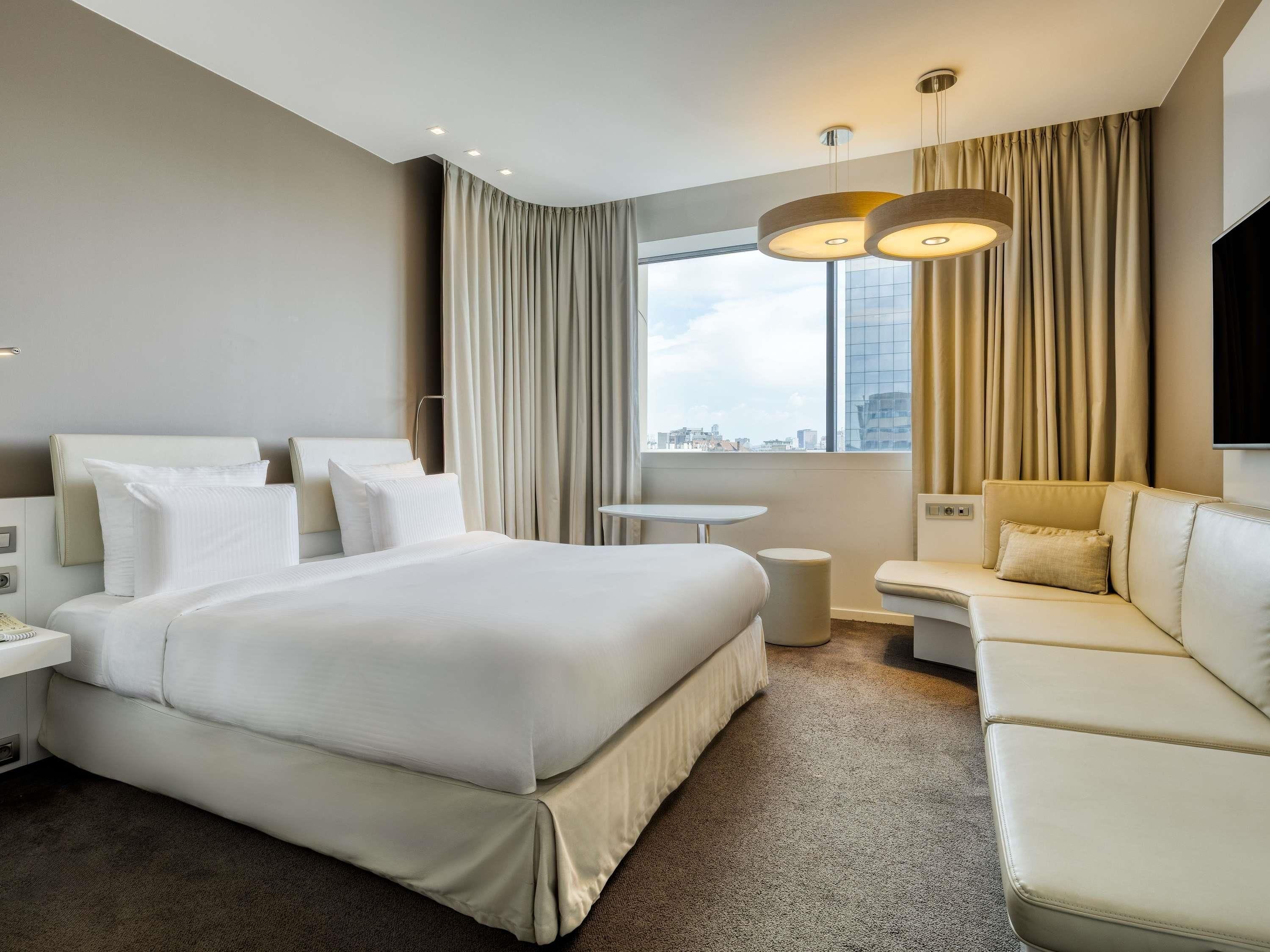 Een hotelkamer met een groot bed, een slaapbank, een klein tafeltje en een televisie.