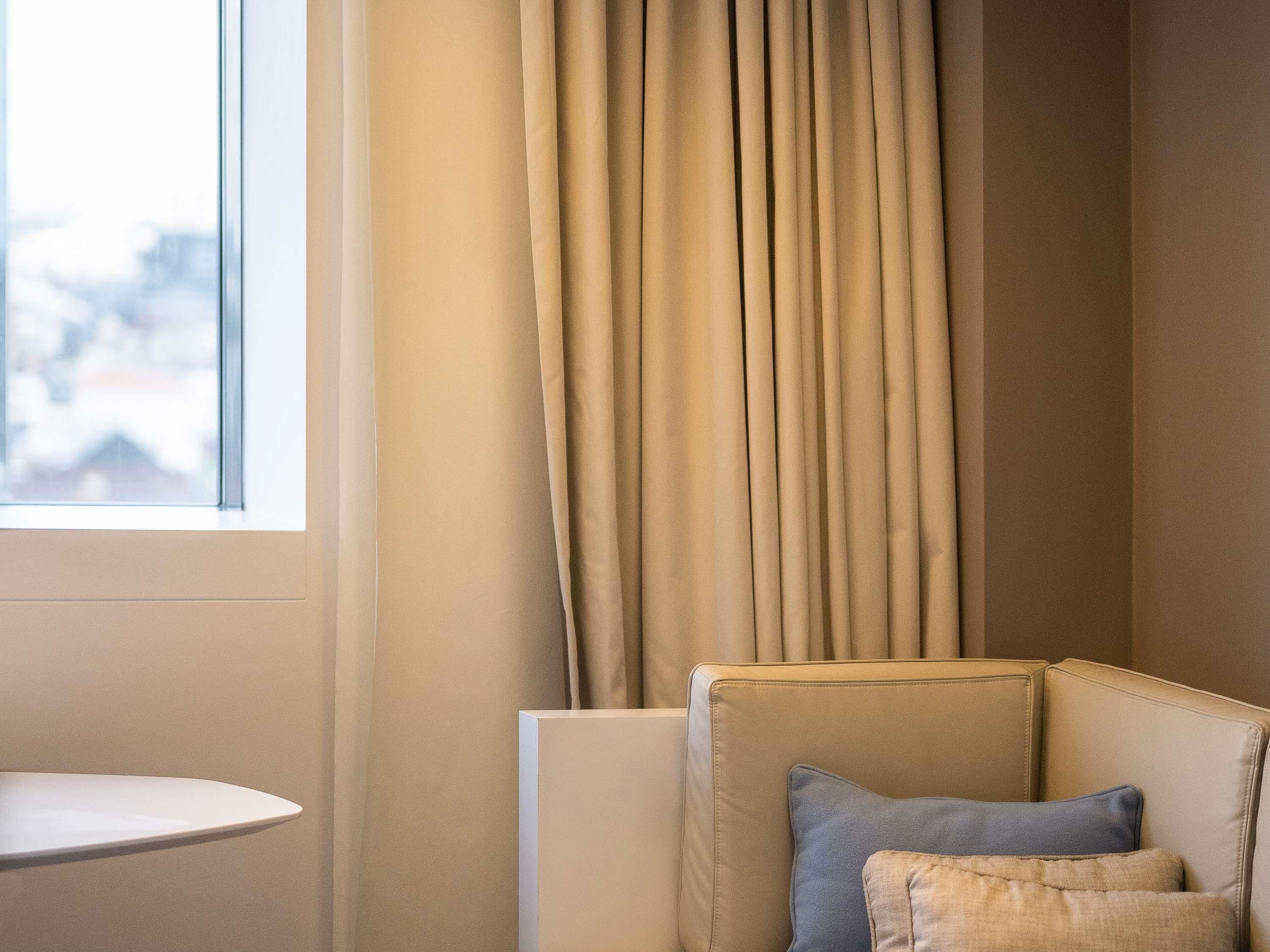A corner of a room with a beige sofa, a small round table, and a window with curtains.