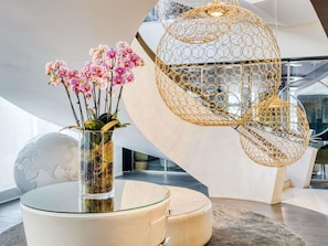 A modern interior with a glass table, a vase with pink orchids, and a unique spherical hanging light fixture. - Pullman Brussels Centre Midi (Brussels)