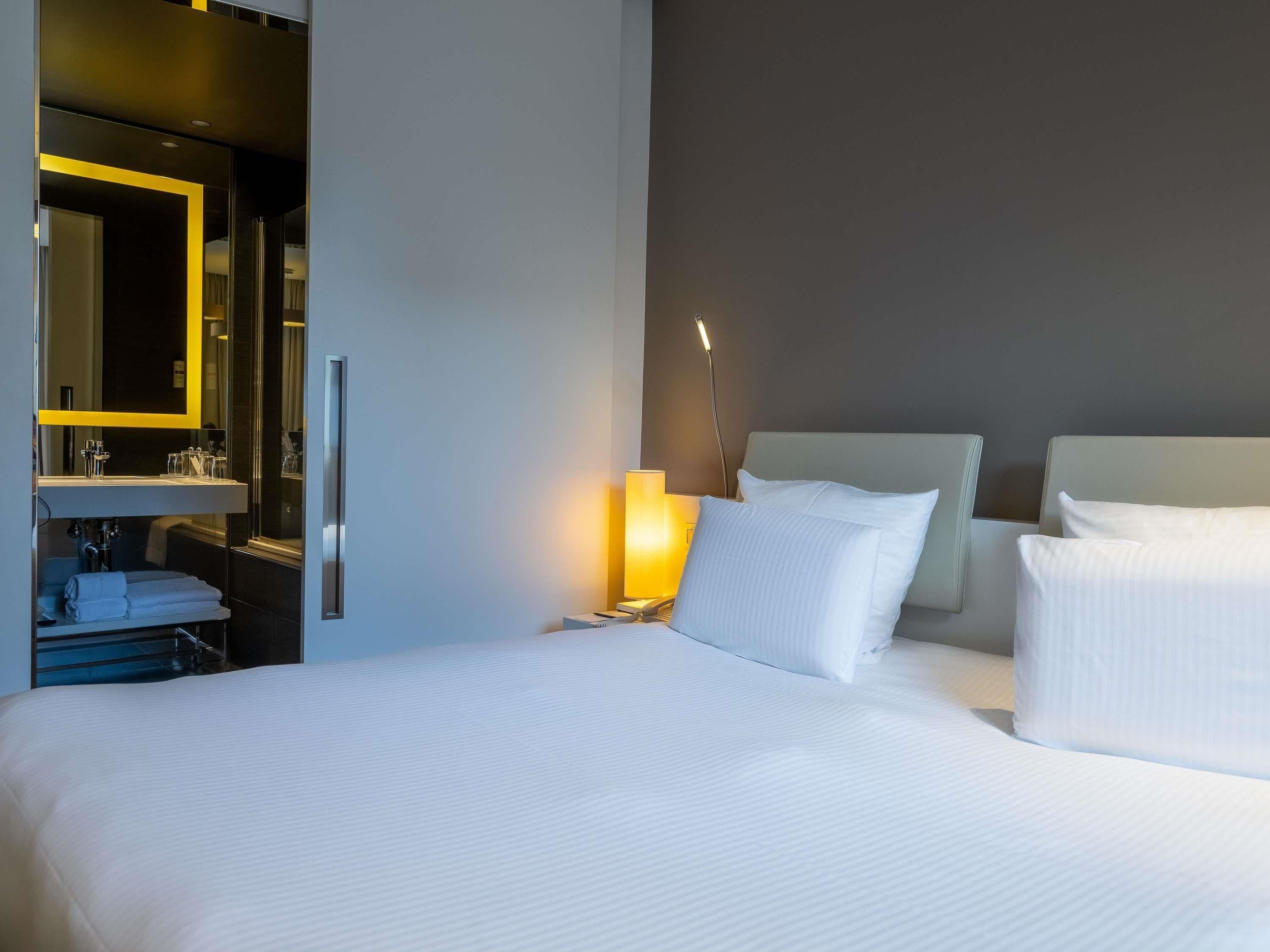 Een hotelkamer met een bed, een bedlamp, een spiegel en een badkamer met een wastafel en handdoekhouder.