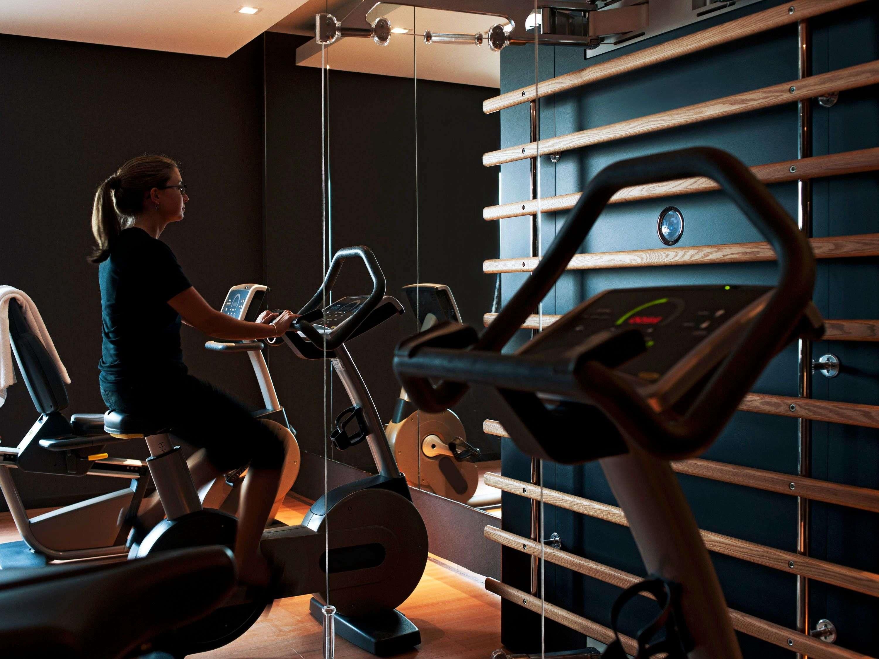A gym with exercise equipment, a wall-mounted rack, and a person using a stationary bike.