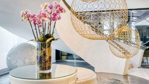 A modern interior with a glass table, a vase with pink orchids, and a unique spherical hanging light fixture. - Pullman Brussels Centre Midi (Brussels)