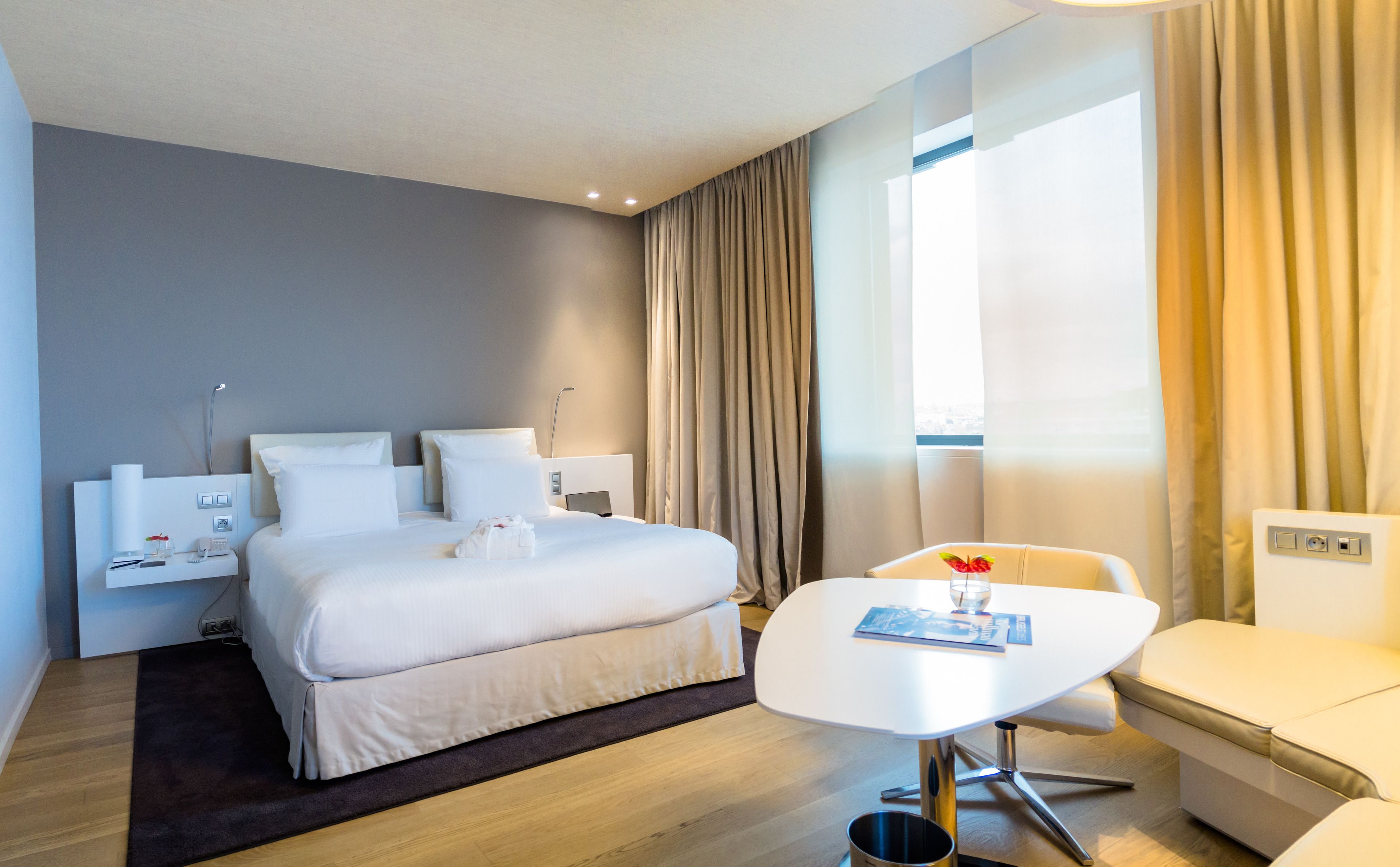 Una habitación de hotel moderna con una cama grande, mesitas de noche, un escritorio y una silla.