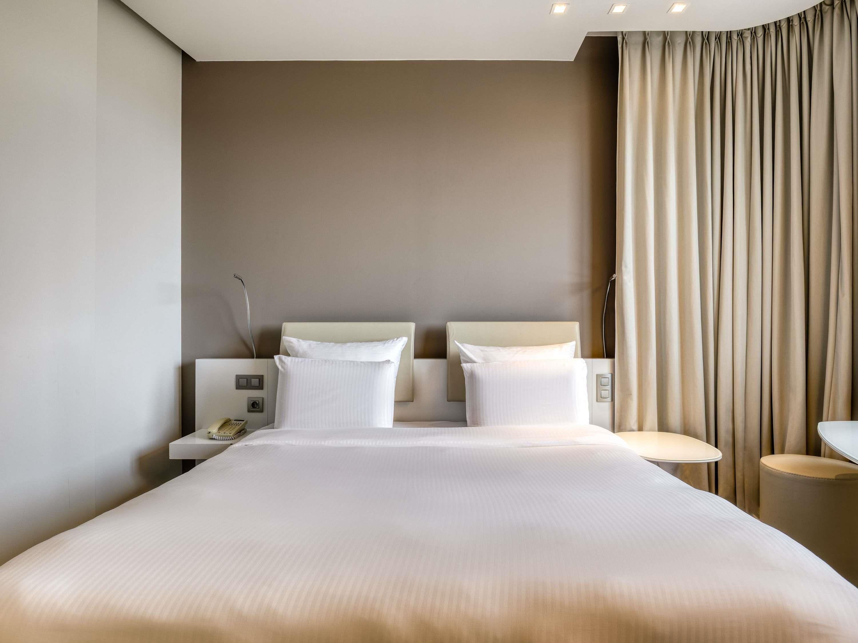 Une chambre d’hôtel avec un grand lit, deux tables de chevet, une lampe de chevet et un rideau.