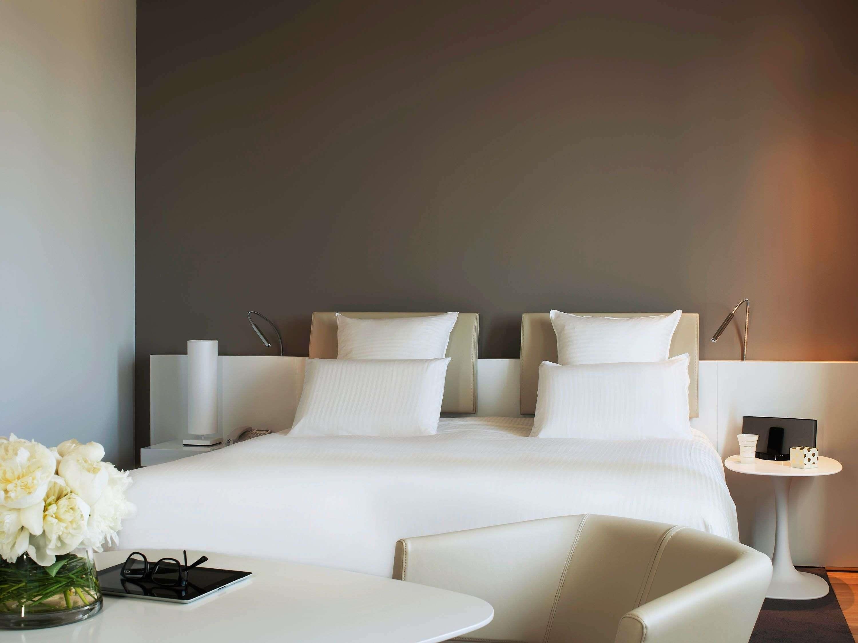 A modern hotel room with a large bed, bedside tables, a small round table, and a chair.