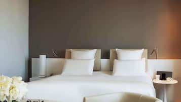 A modern hotel room with a large bed, bedside tables, a small round table, and a chair.