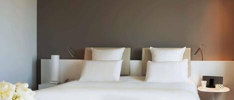 A modern hotel room with a large bed, bedside tables, a small round table, and a chair.