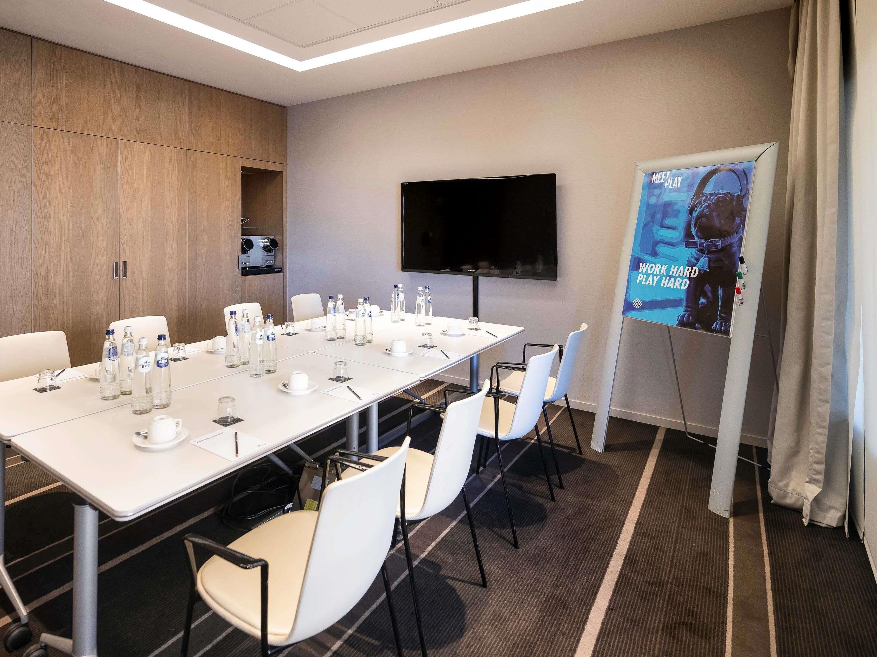 A conference room with a long table, chairs, water bottles, a projector screen, and a TV.