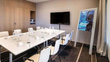 A conference room with a long table, chairs, water bottles, a projector screen, and a TV.