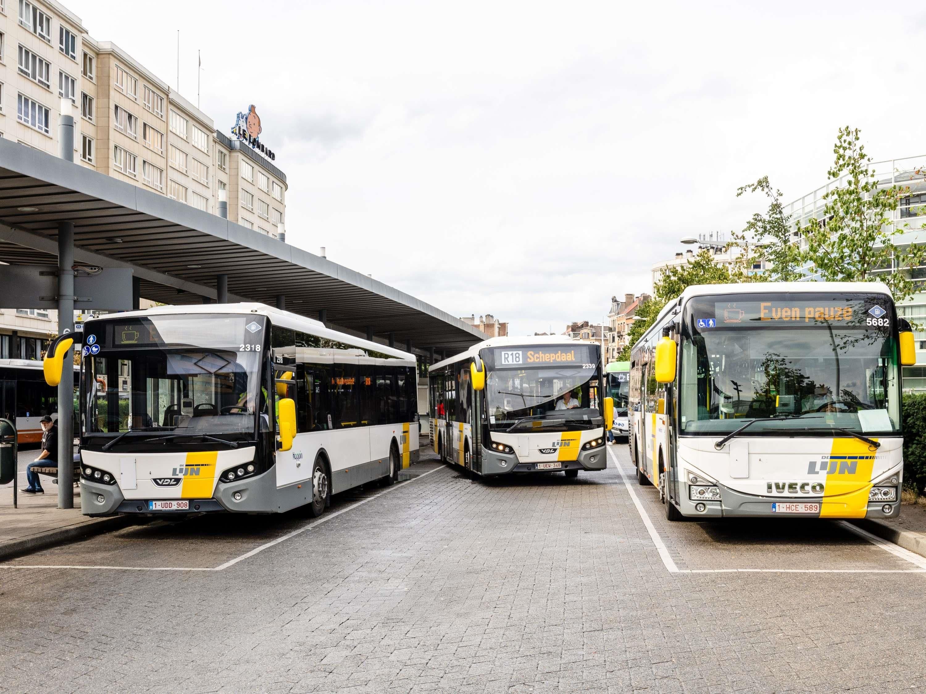 Una estación de autobuses con varios autobuses estacionados, un pasillo peatonal cubierto y edificios al fondo.