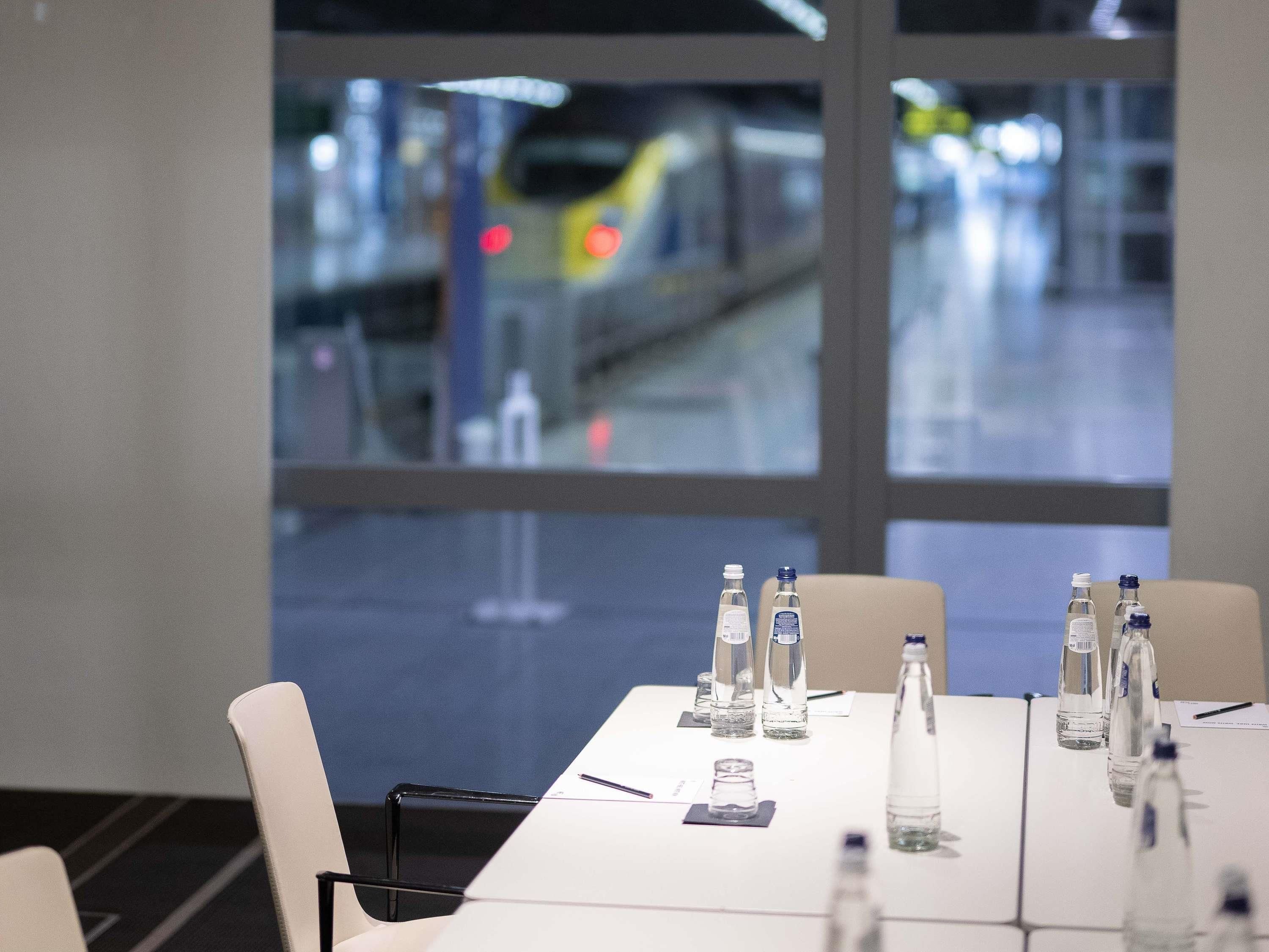Uma sala de conferências com uma mesa preparada para reuniões, uma janela com vista para um trem e um copo d'água sobre a mesa.
