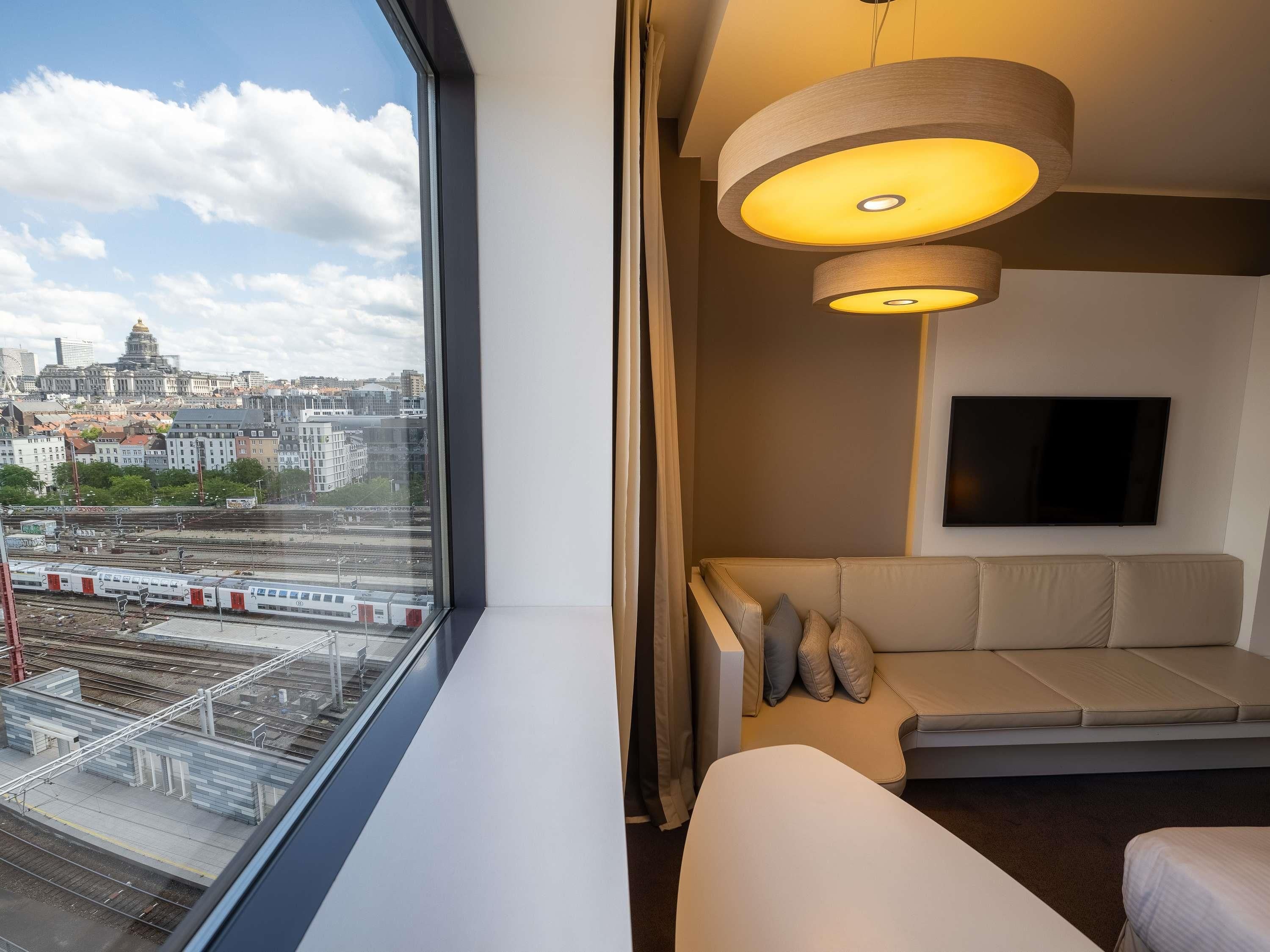 Une chambre d’hôtel moderne dotée d’une grande fenêtre donnant sur la ville, d’un canapé, d’un téléviseur à écran plat et d’une suspension.