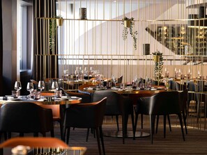 A restaurant with tables set for dining, chairs, and hanging plants. - Pullman Brussels Centre Midi (Brussels)