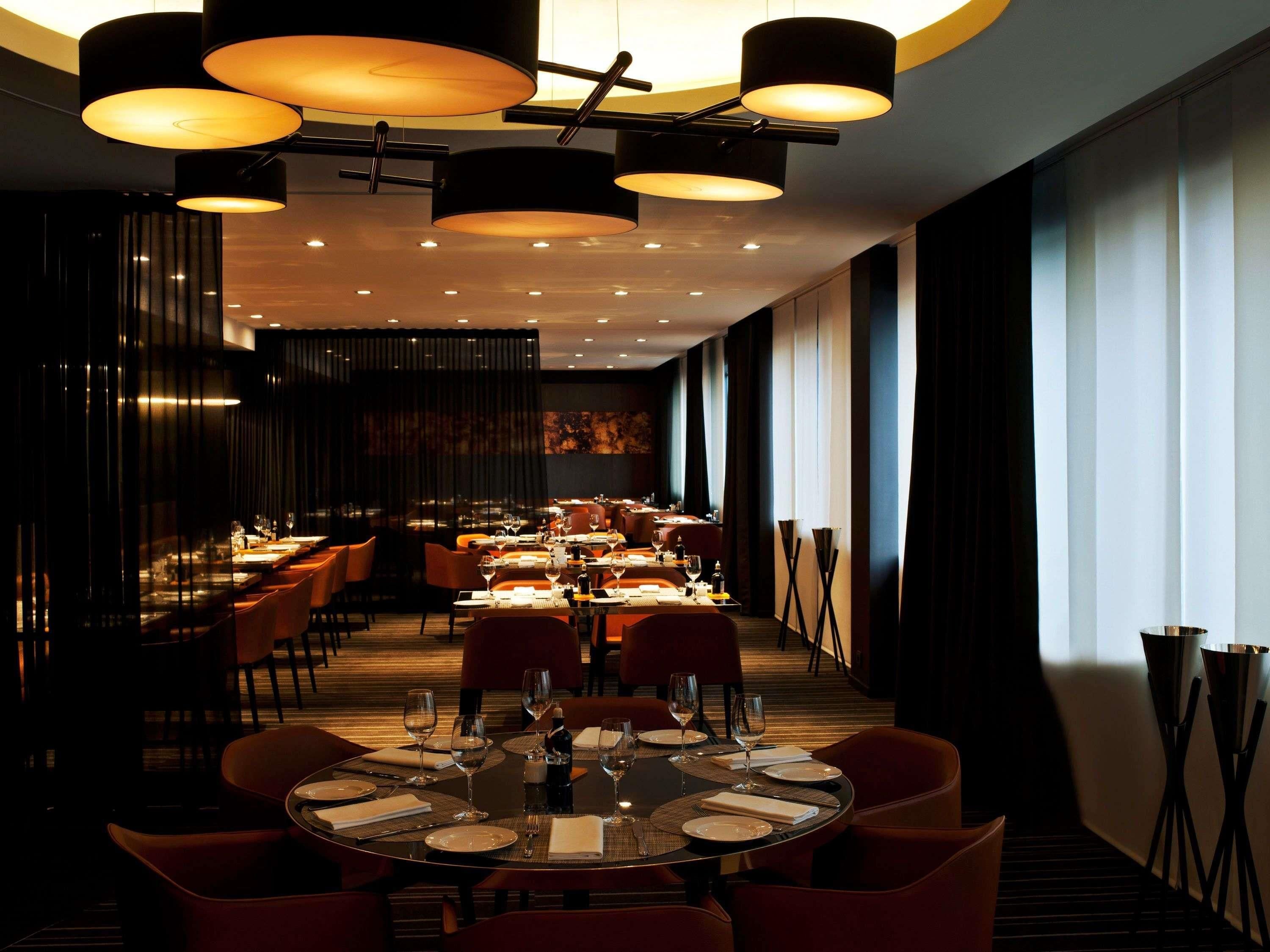 A modern restaurant with round tables, dark chairs, and ambient lighting.