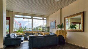 A spacious living room with a large window, a sofa set, a television, and a mirror on the wall. - FF&E Hotel Dania (Fehmarn)