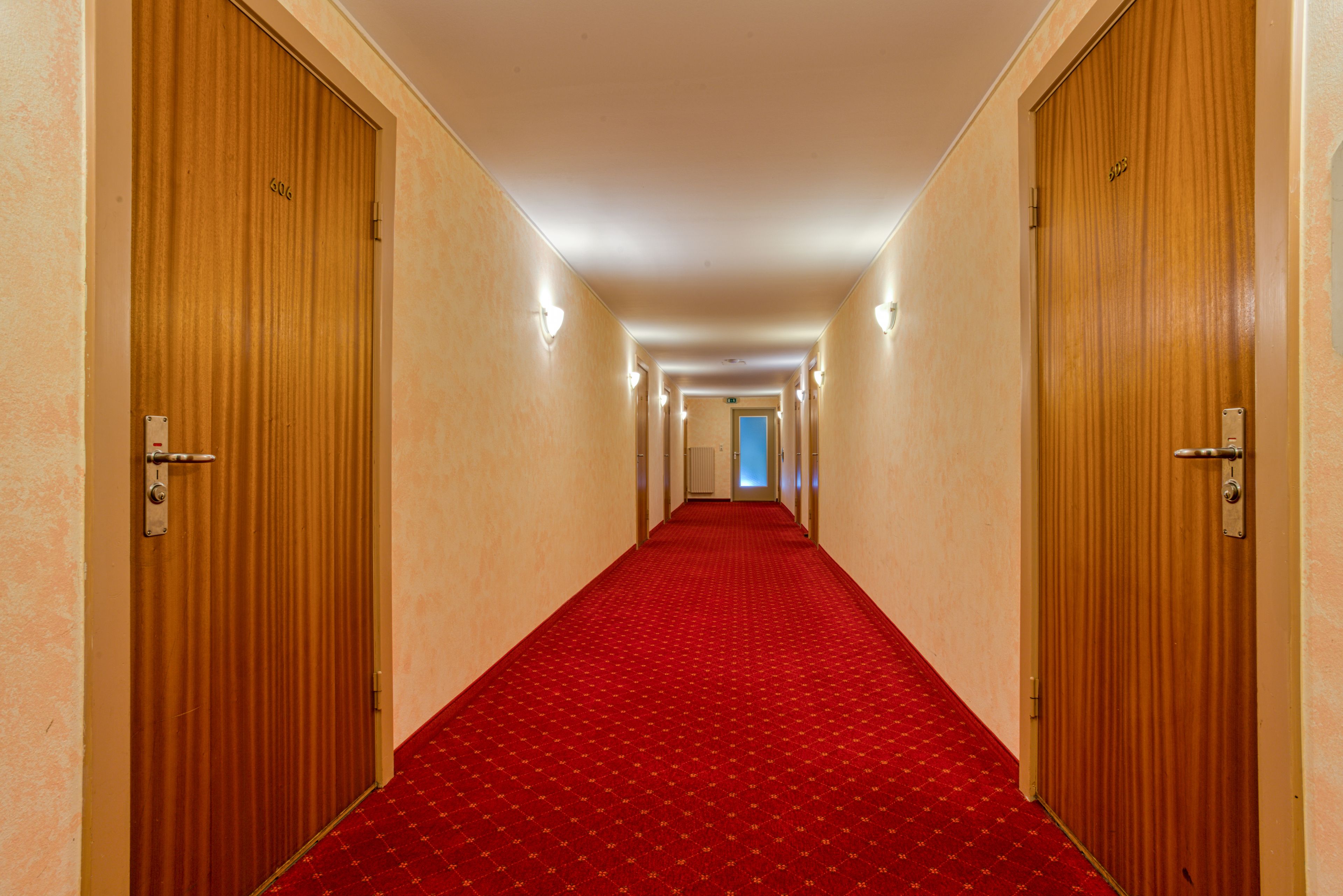 A hallway with wooden doors, a red carpet, and wall sconces.
