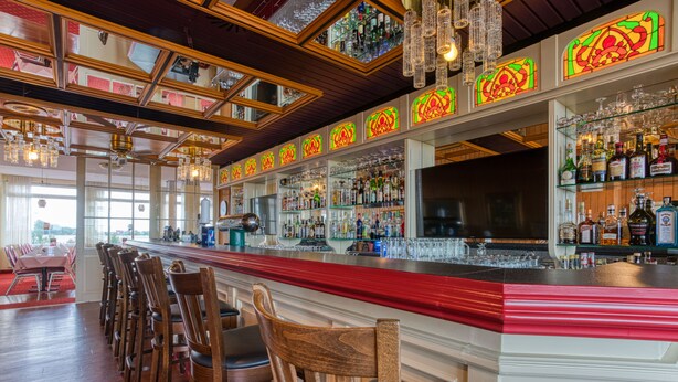 A bar area with wooden chairs, a red bar counter, and various bottles and glasses. - FF&E Hotel Dania (Fehmarn)