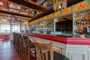 A bar area with wooden chairs, a red bar counter, and various bottles and glasses. - FF&E Hotel Dania (Fehmarn)