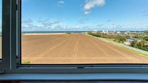 A view through a window of a field, a road, and buildings in the distance. - FF&E Hotel Dania (Fehmarn)
