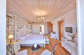 A bedroom with a stone wall, wooden ceiling, a bed, bedside tables, a TV, and a small table with a vase. - Imren Han Hotel - Special Class (Cesme)